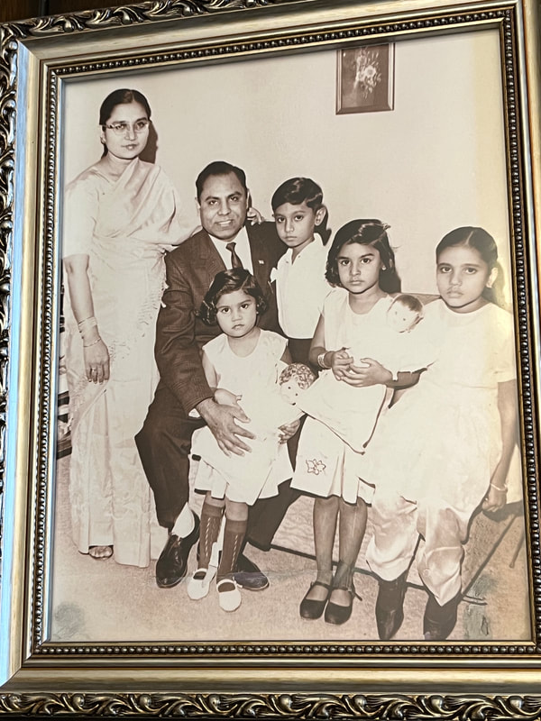 Image of Khan family. three little girls in white dress, one little boy in a white button. Ahmad Khan seated wearing a suit and Salma Khan wearing a sari